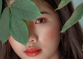 Close-up portrait of a woman peeking through green leaves, showcasing beauty and nature.